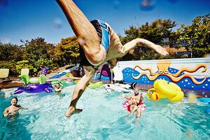 Fotografija Man in mid air jumping into pool during party, Thomas Barwick, (40 x 26.7 cm)