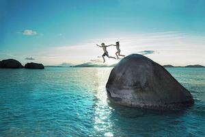 Umjetnička fotografija Two kids holding hands jumping off rock into sea, Gary John Norman, (40 x 26.7 cm)